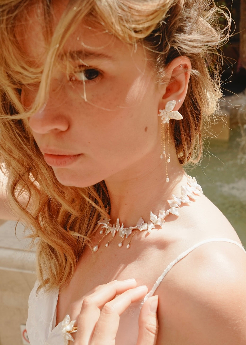 Woman wearing delicate earrings and a necklace with a blurred natural background