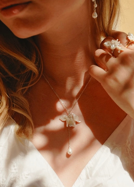 Close-up of a woman wearing a delicate necklace with floral pendant and pearl earrings.