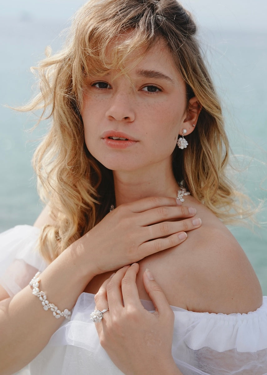 Woman with blonde hair wearing earrings and a bracelet against a light background