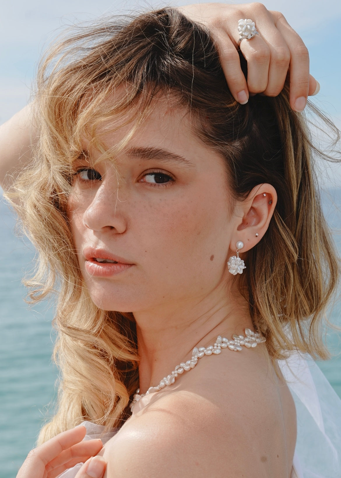Woman with styled hair and pearl jewelry against a blurred natural background