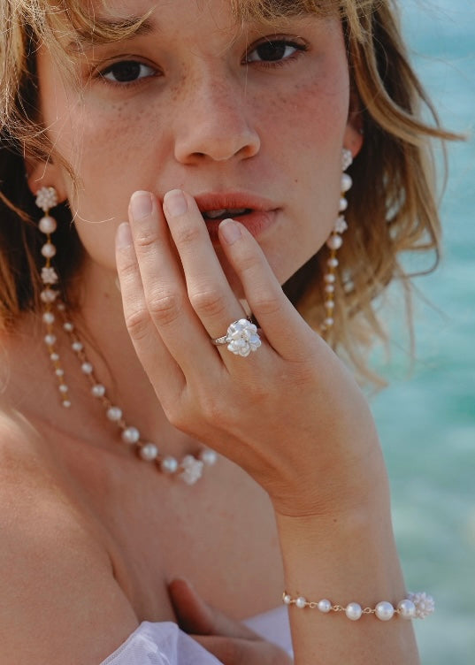 Woman wearing pearls and a ring with a blurred ocean background