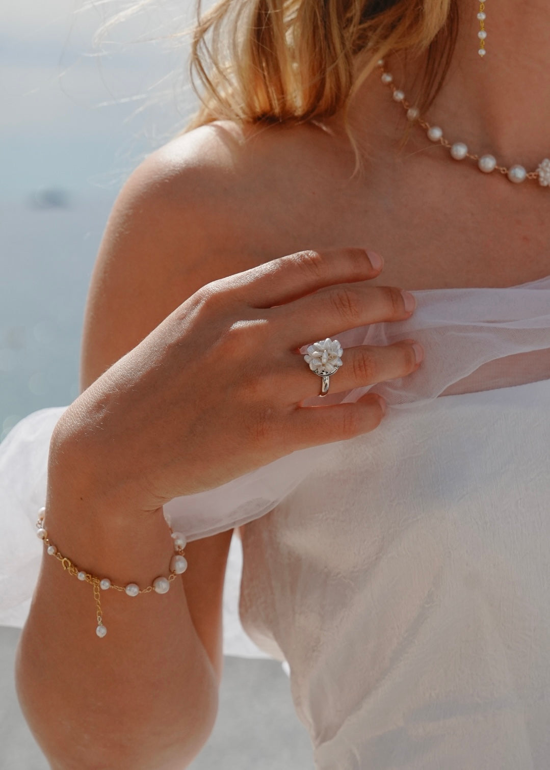 Close-up of a hand wearing a pearl bracelet and ring, with a blurred background.