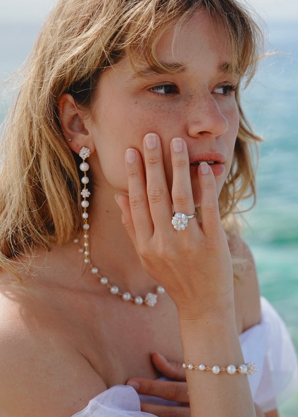 Woman wearing a pearl necklace, earrings, and bracelet with a blurred background