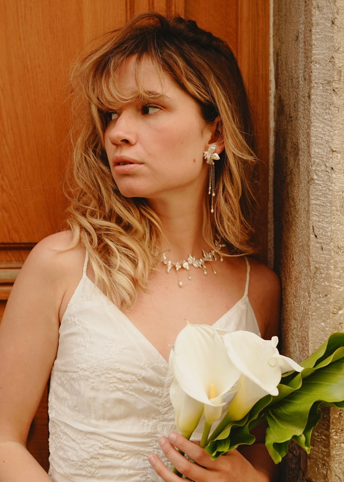 Woman in a white dress holding white flowers against a wooden door.