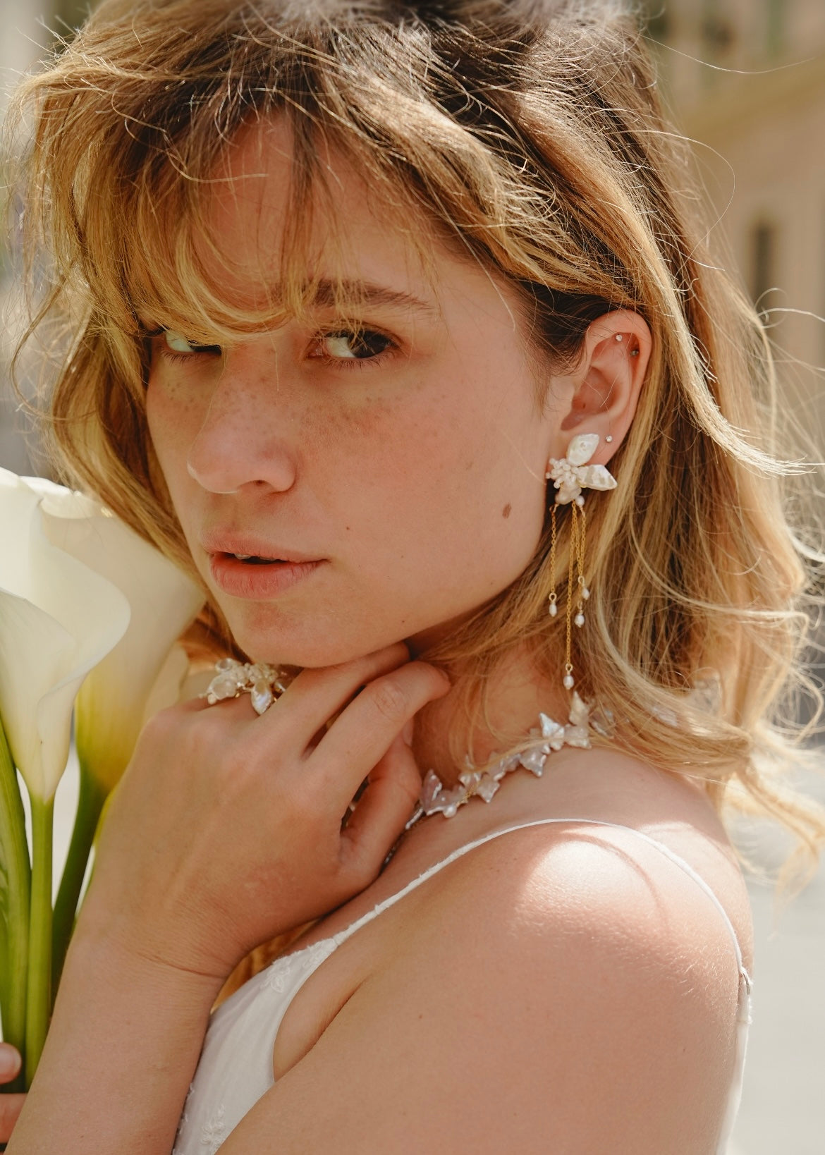 Woman wearing floral earrings and a necklace, holding flowers.