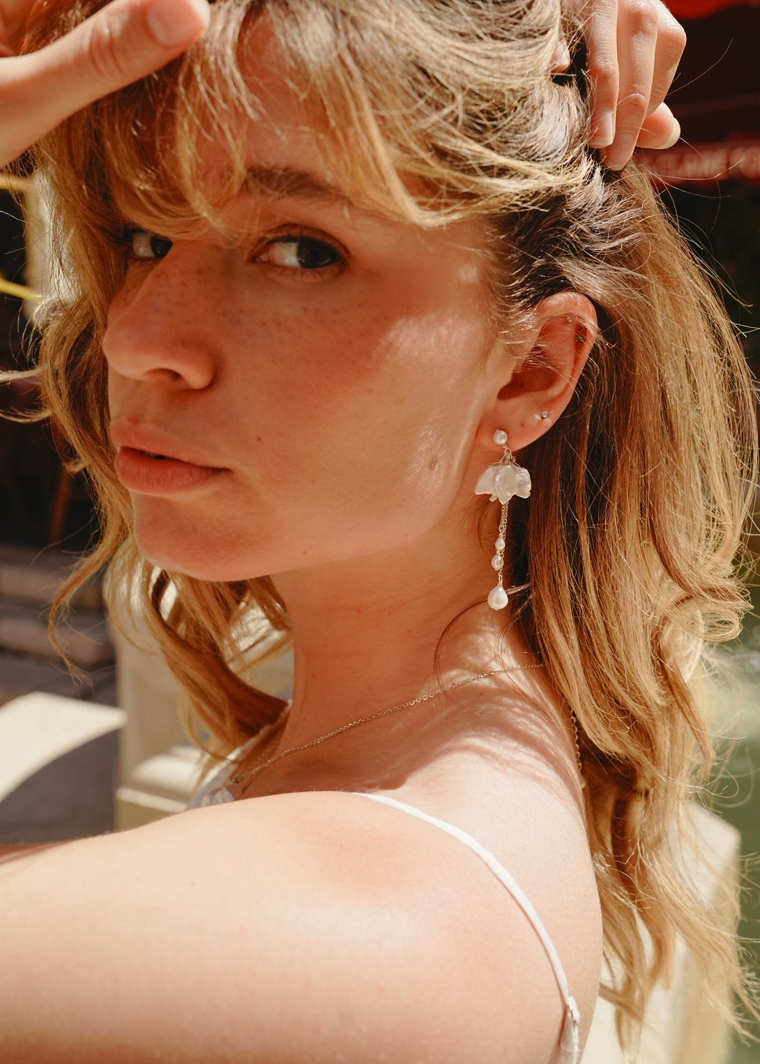 Woman with blonde hair and earrings, wearing a white top.