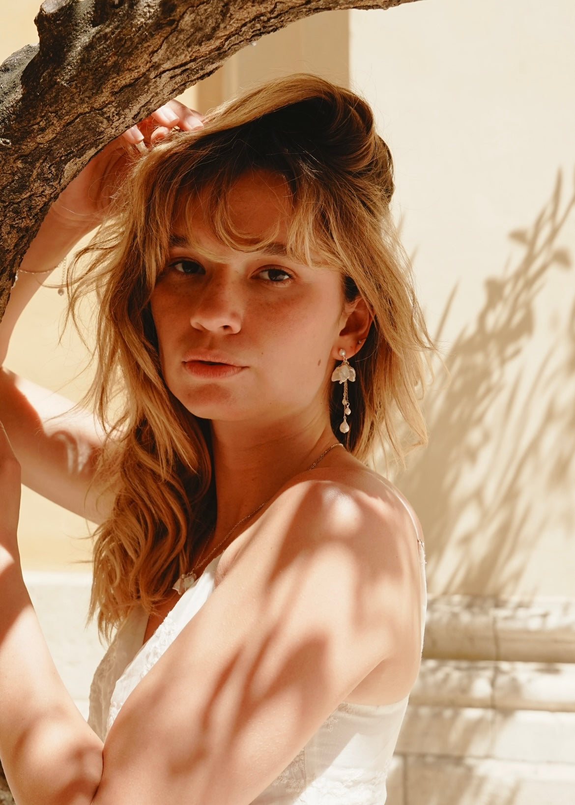 Woman with blonde hair and earrings standing next to a tree