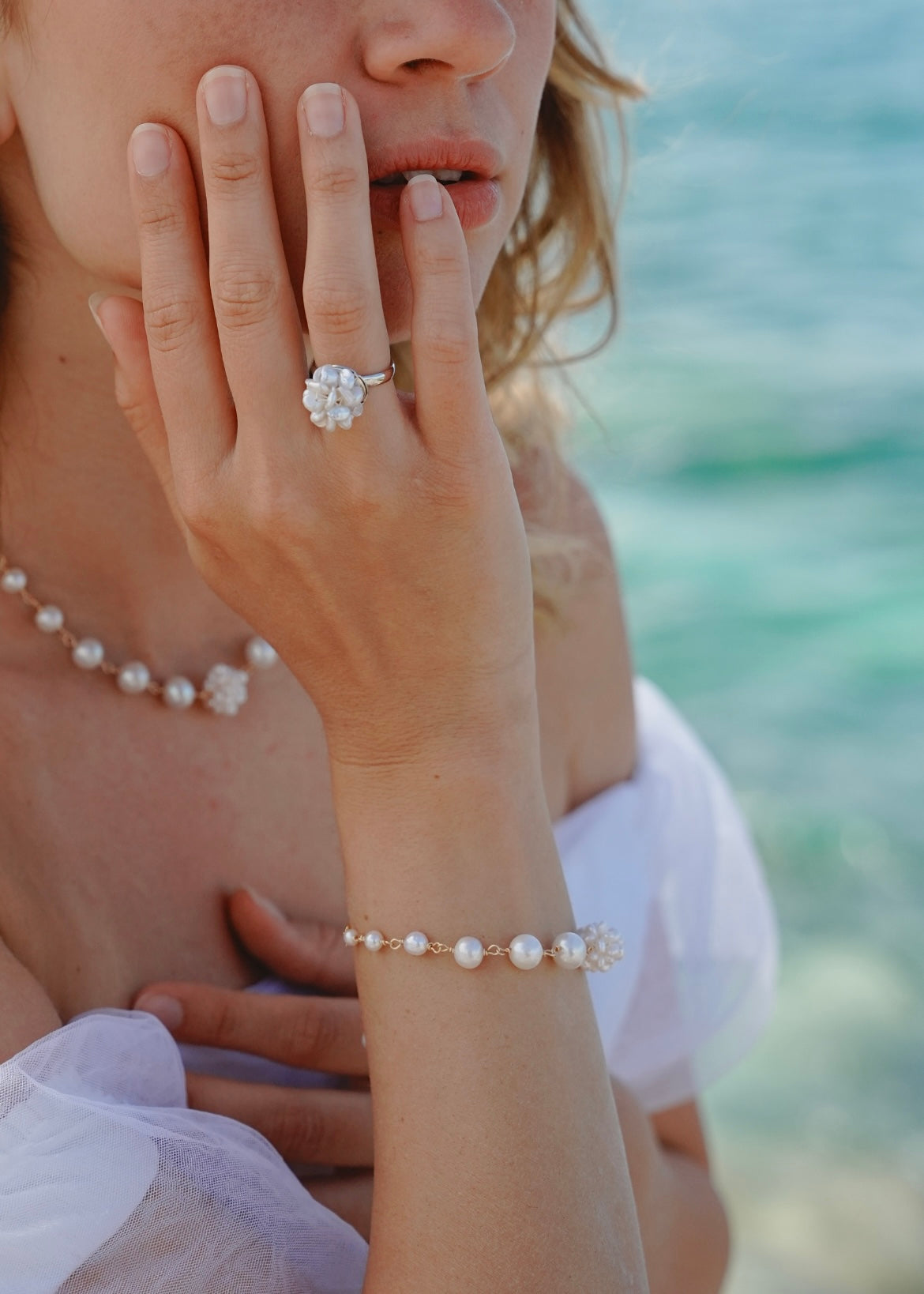 Close-up of a person's hand wearing a pearl bracelet and ring with a blurred background