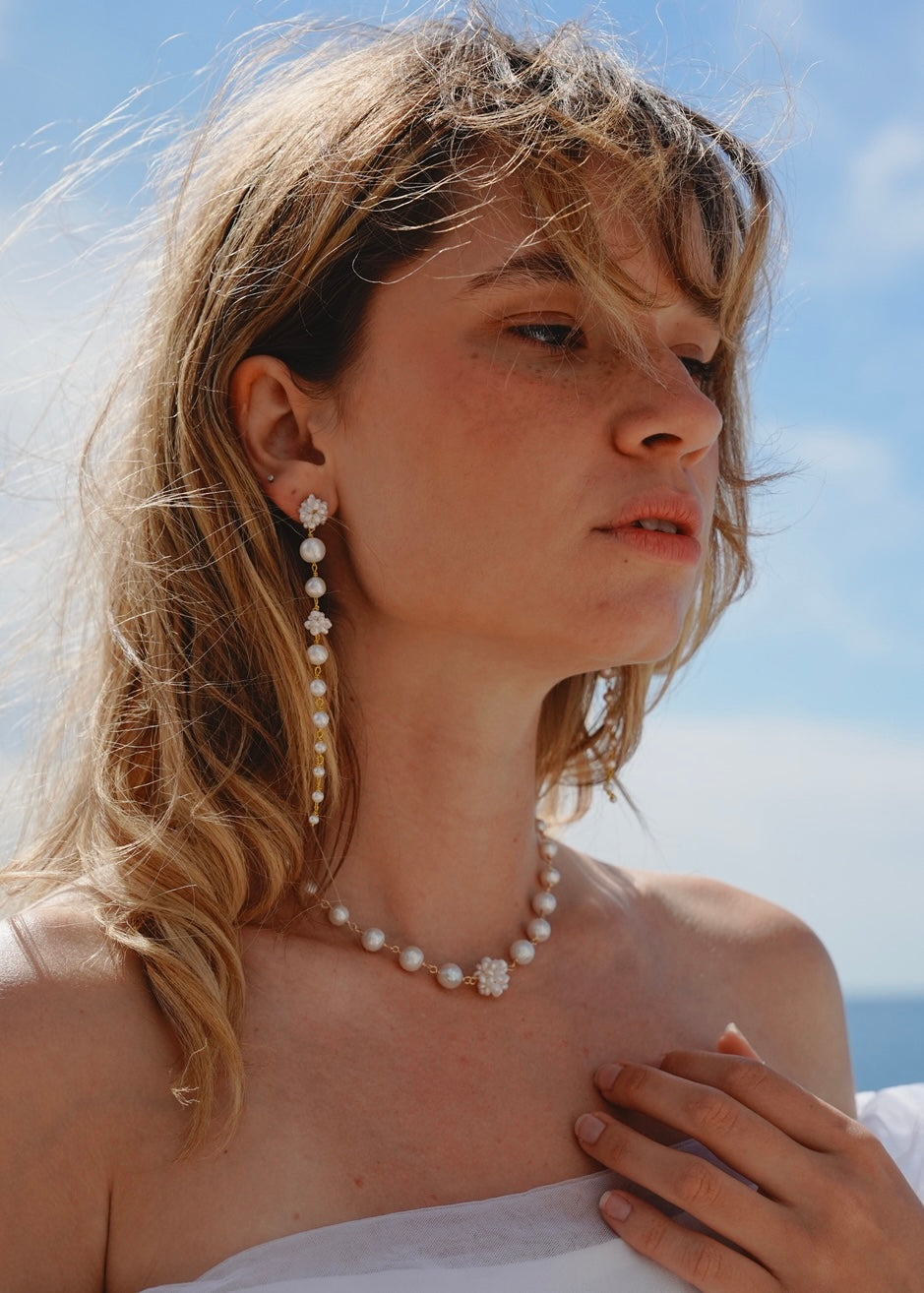 Woman wearing a pearl necklace and earrings with a clear blue sky background