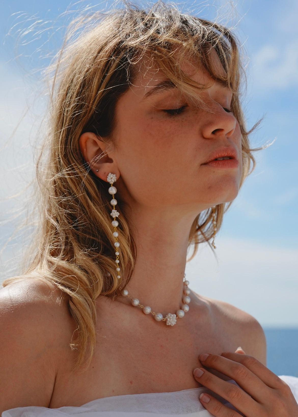 Woman wearing a pearl necklace and earrings with a clear blue sky background
