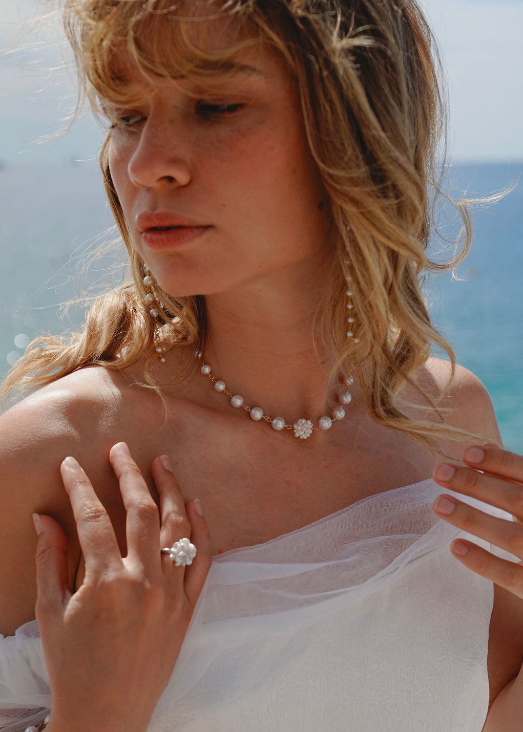 Woman wearing a pearl necklace and ring with a blurred natural background