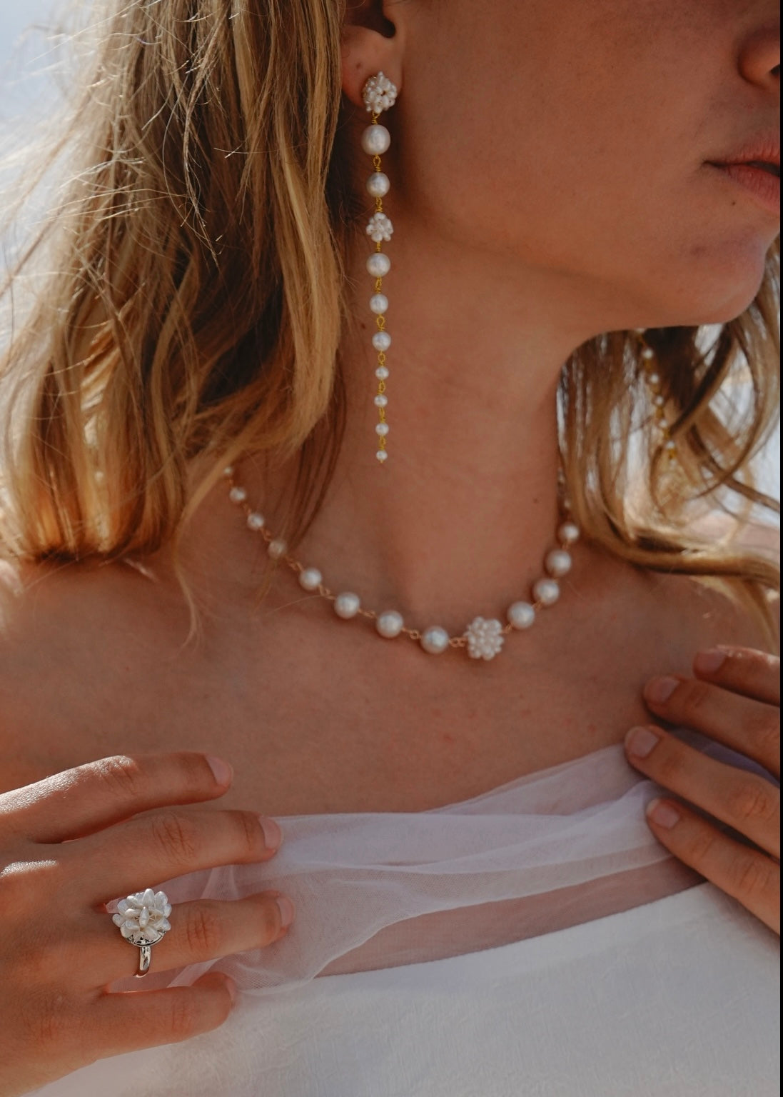 Close-up of a person wearing a pearl necklace and earrings with a blurred background