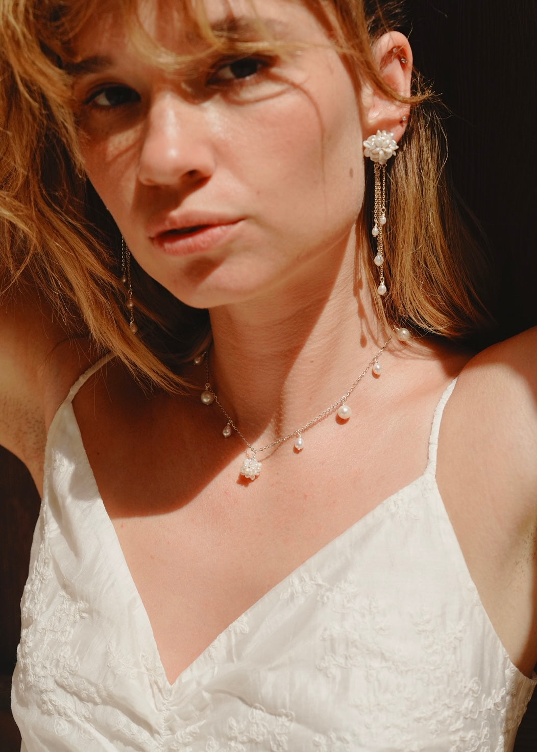 Woman wearing a white dress with pearl jewelry against a dark background