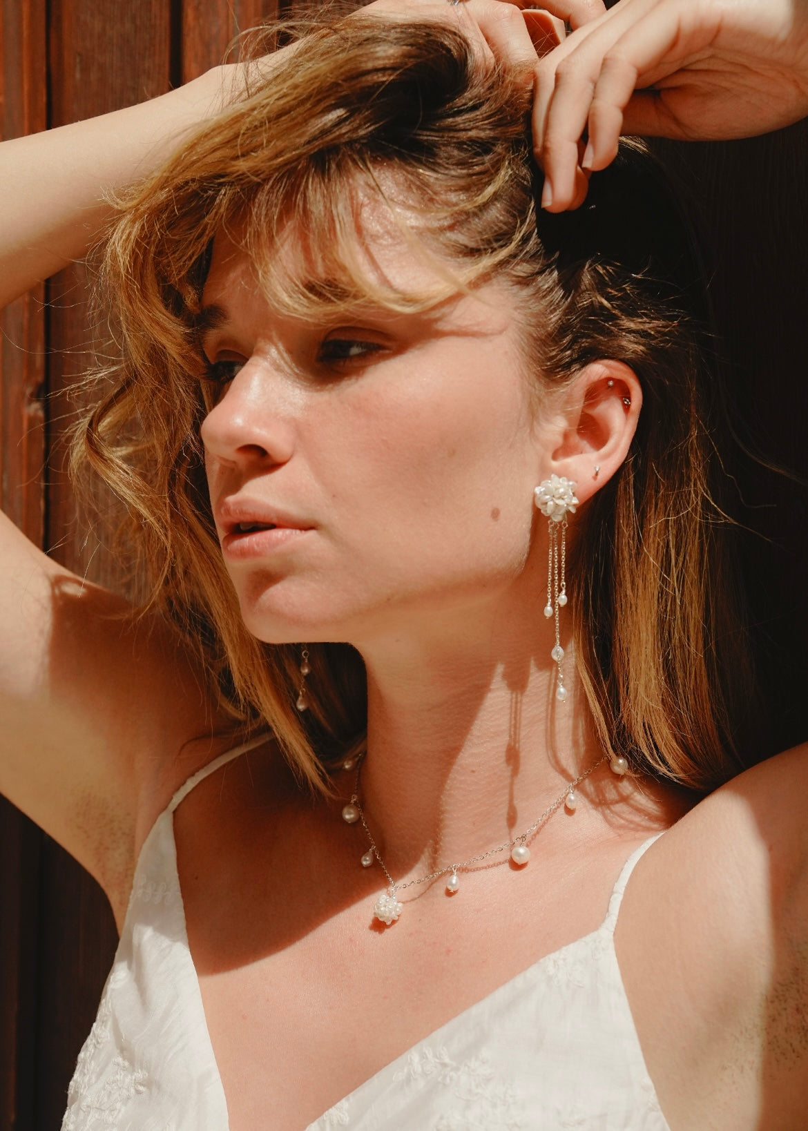 Woman with styled hair and pearl jewelry against a wooden background