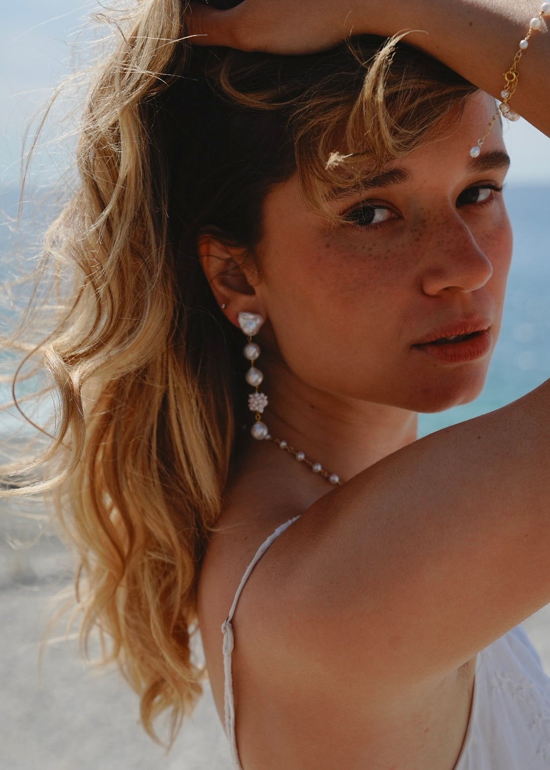 Woman with styled hair and jewelry against a blurred natural background