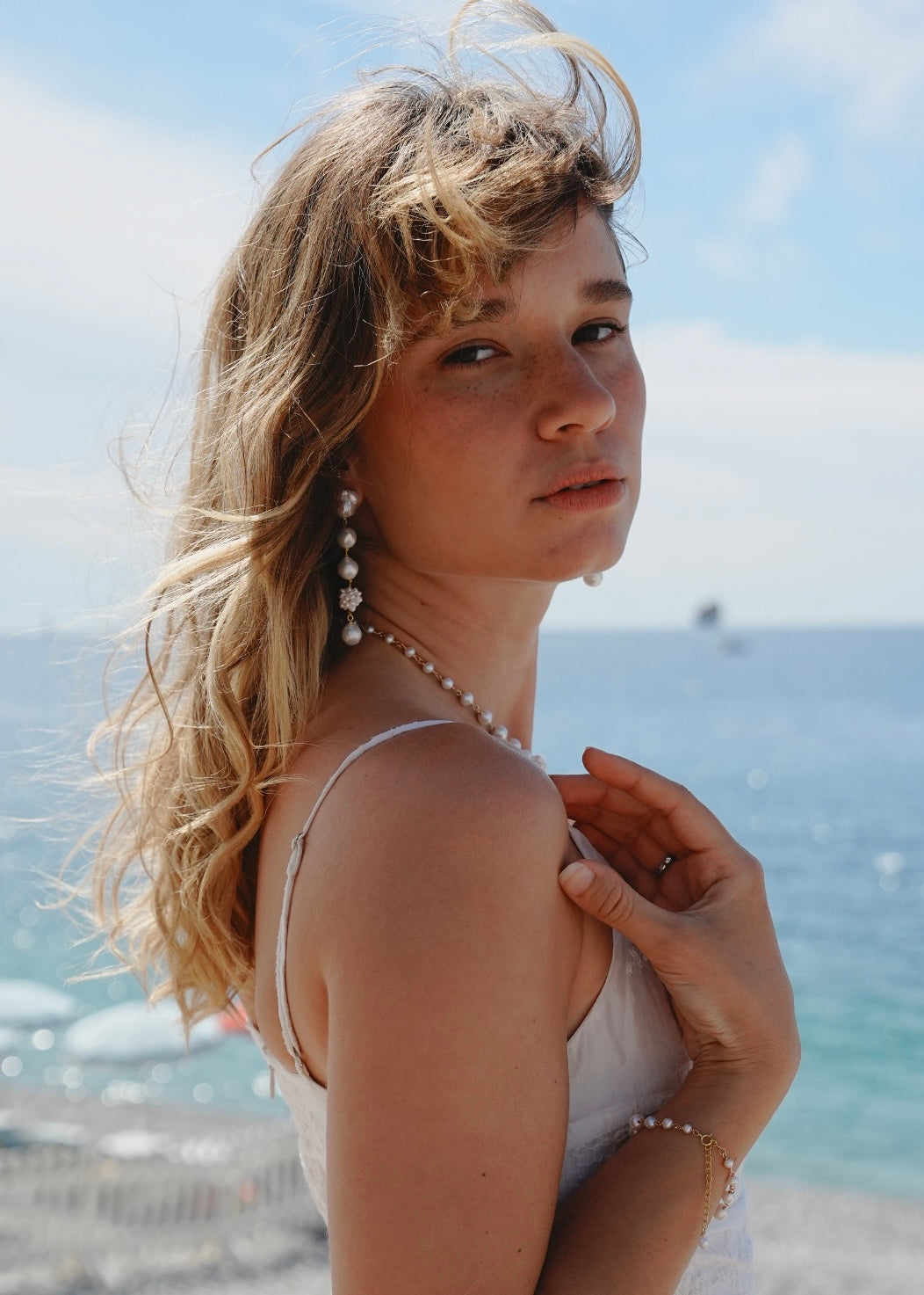Woman with blonde hair and pearl necklace by the ocean
